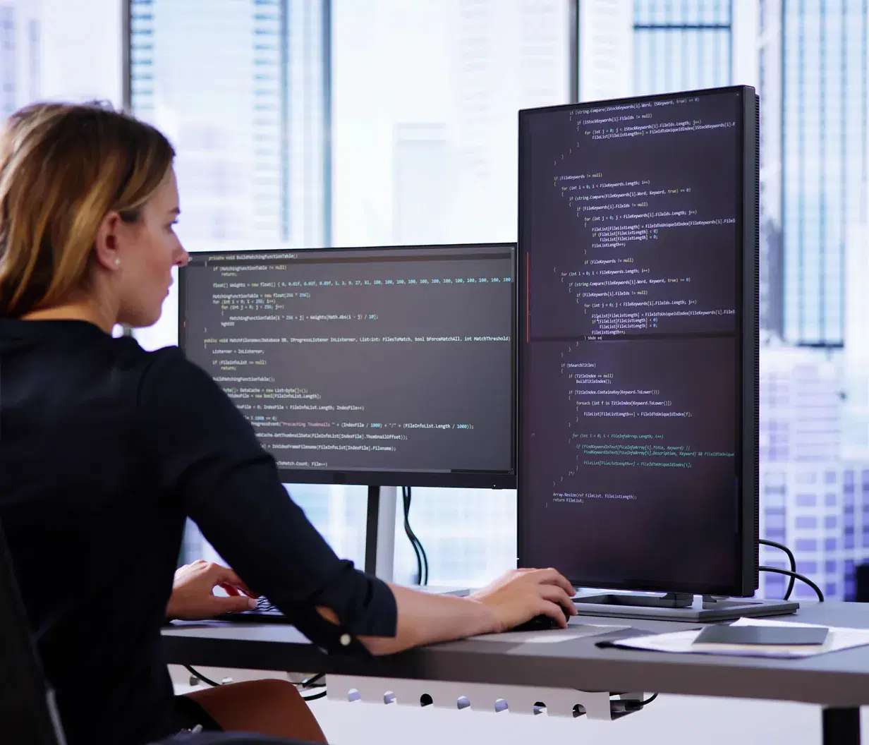 Municipal staffer working at a dual-monitor workstation writing automation code