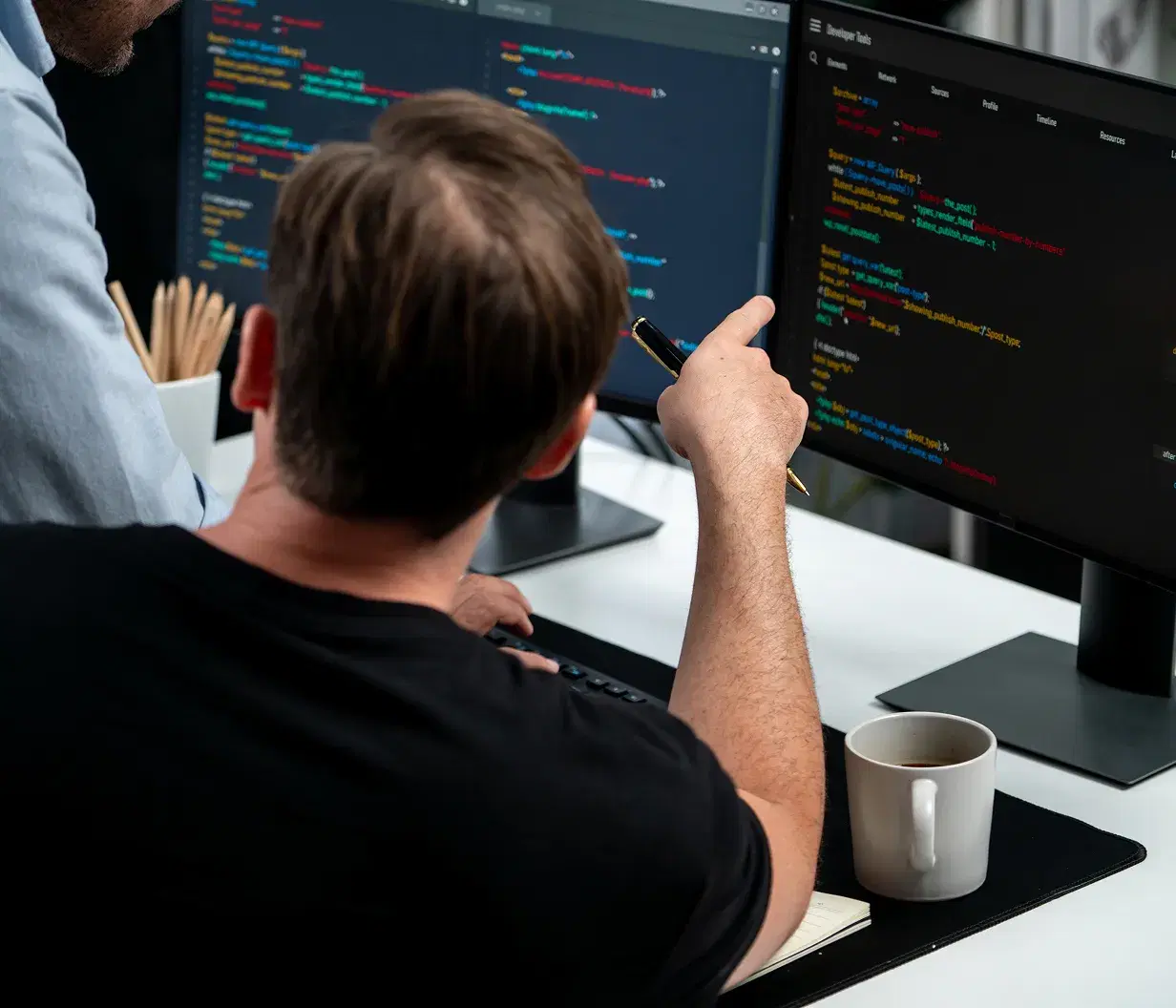 Two developers reviewing code together across multiple monitors